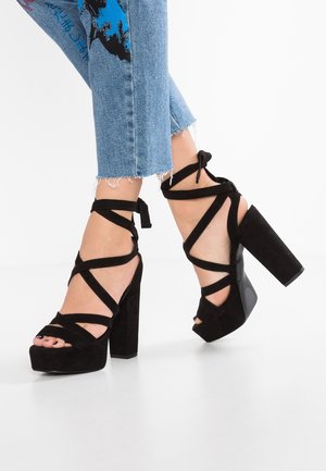 Des pieds chaussés de sandales à plateforme noires à talons hauts avec des brides autour des chevilles et un jean cropped bleu clair avec des ourlets effilochés et un imprimé graphique.