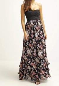 Vestido maxi con un corpete negro ajustado, falda acampanada de flores en negro, rosa y crema, con volantes y un diseño sin tirantes.