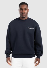Sudadera azul marino hecha de una mezcla de algodón; cuenta con un cuello redondo acanalado, mangas con puños y un pequeño logo blanco en el pecho.