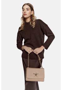 Maglione lavorato a maglia marrone con maniche lunghe, abbinato a una gonna marrone. Una borsa a tracolla color beige chiaro presenta un accento a forma di stella e una tracolla a catena.