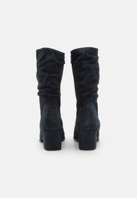 Dark blue suede knee-high boots with a slouchy design, square high heels, and soft texture. Back view features minimal hardware details.