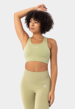 Olivroheline ribadega spordibra, millel on lõikekujundus ja logo keskel, koos kõrge vöökoha ja sama tooni retuusidega, millel on väike logo.