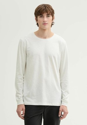 Chemise à manches longues gris clair avec un col rond, texture lisse et design minimaliste, associée à un pantalon noir.