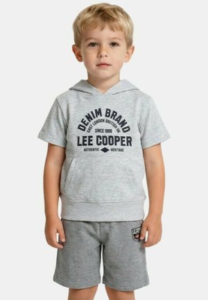 Garçon blond portant un sweat à capuche gris clair à manches courtes avec l'inscription "Lee Cooper" et un short gris assorti avec un patch logo, debout face à l'avant.