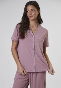 Conjunto de pijama de manga corta en color rosa, hecho de tela suave, que incluye una camisa de botones con ribete, detalle de bolsillo y pantalones holgados a juego.