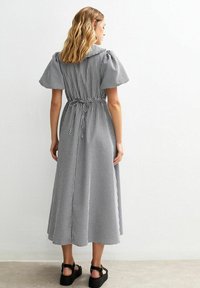 Robe midi à carreaux vichy noir et blanc avec des manches bouffantes, une taille cintrée et un détail à nouer. Le mannequin porte des sandales noires à semelles épaisses.