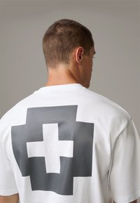 Weißes T-Shirt mit einem großen schwarzen gepunkteten Kreuzdesign auf dem Rücken. Einfach, kurze Ärmel mit rundem Halsausschnitt. Weiche Textur.