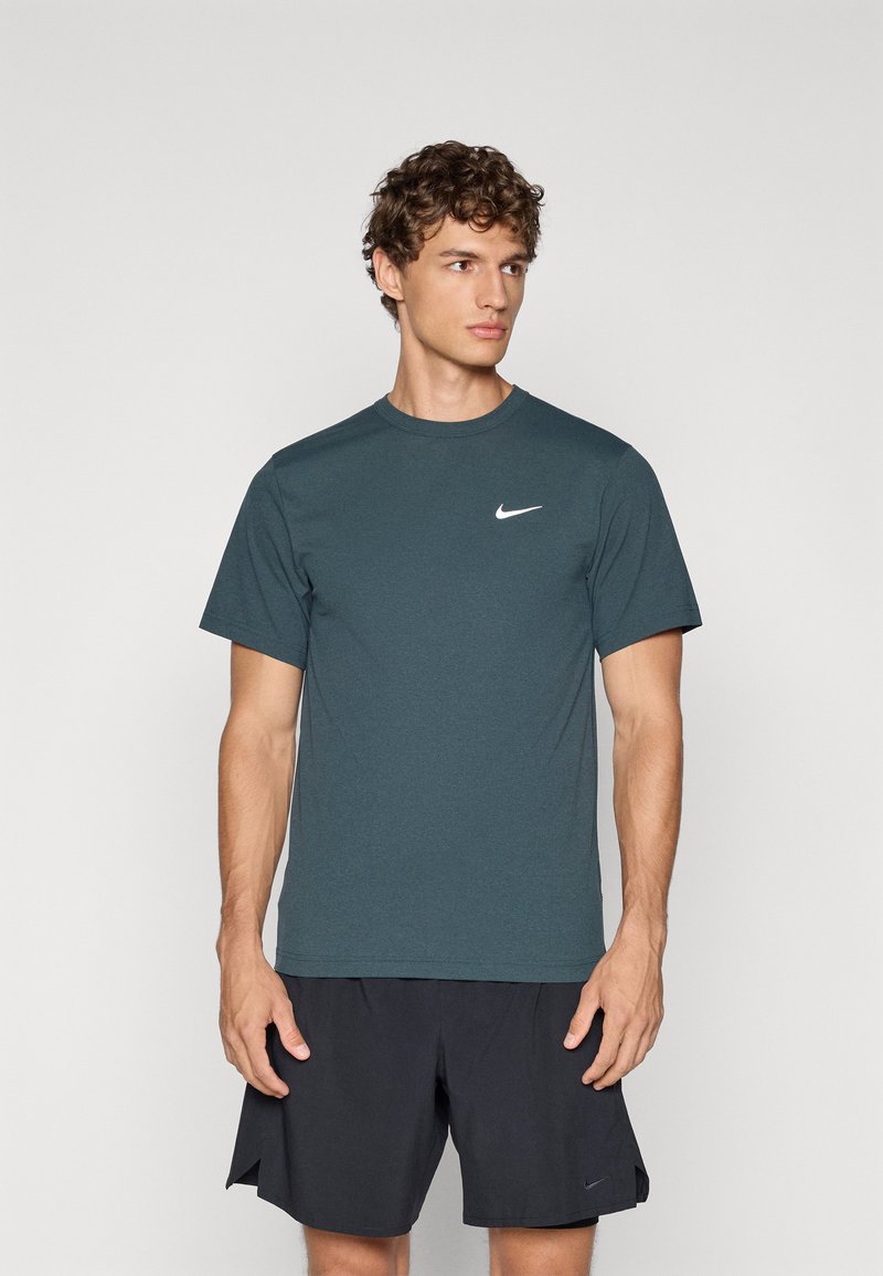 Mørk teal Nike kortermet treningstrøye i glatt stoff, med en hvit logo på brystet, sammen med svarte shorts.