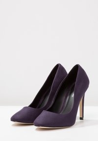 Escarpins en daim violet à talon haut présentant un bout pointu et un talon stiletto fin, avec une texture lisse et un design minimaliste.