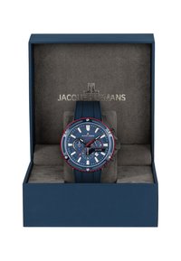 Blå sportklocka med en texturerad urtavla, vita timmarkörer och röda accenter. Presenteras i en blå låda med grå insida.