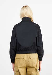 Schwarze Bomberjacke mit hohem Kragen, elastischem Bund und gerippten Bündchen. Hergestellt aus glattem Stoff, getragen über beigen Cargo-Hosen.
