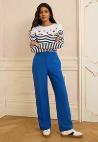 Haut rayé à manches longues avec broderie colorée, assorti à un pantalon large bleu royal et des baskets blanches avec semelles marron.