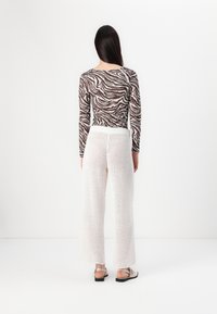 Top de manga larga con estampado de cebra en marrón y blanco; pantalones de punto amplios y blancos; sandalias planas con tira y suela negra.