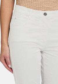 Pantalon en coton blanc avec poches avant, fermeture à bouton argenté et texture lisse. Présente un design ajusté au niveau des hanches.