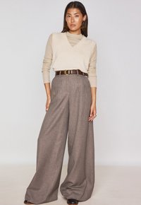 Maglione beige a scollo a V sovrapposto a un dolcevita beige, abbinato a pantaloni a quadri marroni a vita alta e gamba larga, con una cintura marrone.