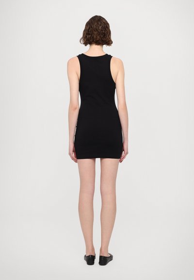 Robe noire sans manches avec un design ajusté, longueur genou, texture lisse et décolleté rond. Portée avec des ballerines noires.