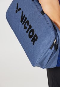 Blå tygsportväska med svart "VICTOR"-logotyp, dragkedjestängning och texturerad yta. Har dubbla sidofickor och ett robust handtag.