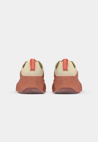 Sneakers with a beige upper, red heel tab, and textured red rubber sole. Features a rounded shape and minimalistic design.
