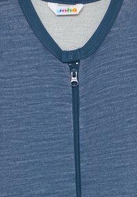 Modré zipsové oblečenie s textúrovanou tkaninou a okrúhlym výstrihom. Obsahuje strieborný zips a farebnú označovaciu etiketu vo vnútri goliera.