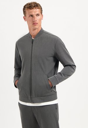 Grijze zip-up jack met een staande kraag, lange mouwen, zijzakken en omgeslagen manchetten. Gemaakt van textiel met een subtiel patroon.