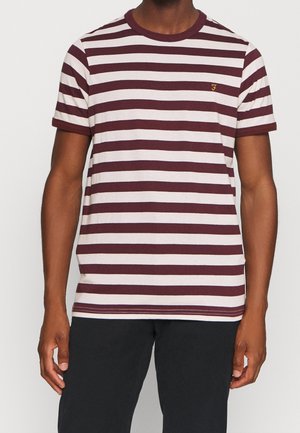 Homme portant un t-shirt à manches courtes rayé horizontalement en bordeaux et blanc avec un petit logo "F" doré sur la poitrine et un pantalon noir.