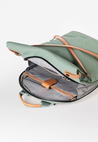 Zaino verde con una superficie liscia e accenti in pelle color nocciola. L'interno presenta una fodera a fantasia grigia e un dettaglio di cinghie per l'organizzazione.