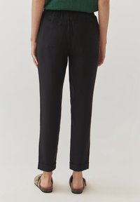 Schwarze Hose mit lässiger Passform, mit umgeschlagenen Säumen und elastischem Bund. Verfügt über zwei Gesäßtaschen und eine glatte, matte Textur.