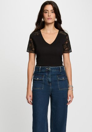 Zwarte V-hals top met korte kanten mouwen, gecombineerd met donkerblauwe high-waisted wijde jeans met voorzakken en zichtbare stiksels.