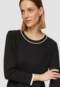 Zwarte trui met een ronde halslijn en witte accenten. Lange mouwen met witte details bij de manchetten. Zachte, gestructureerde stof.