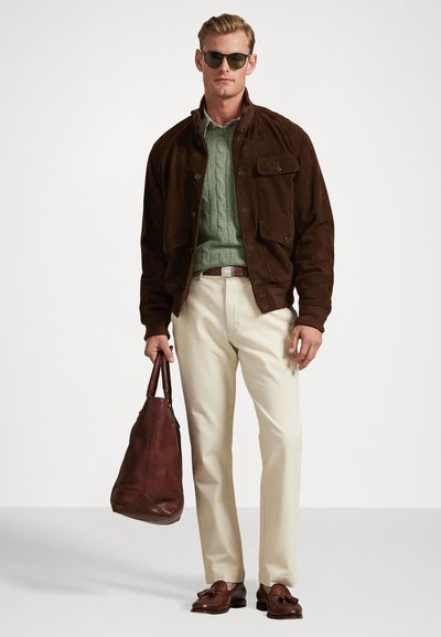 Καφετί σουέτ μπουφάν πάνω από ένα πράσινο πλεκτό πουλόβερ, κρέμα παντελόνι, καφέ δερμάτινες loafers και μια καφέ δερμάτινη τσάντα. Φορετά γυαλιά ηλίου.