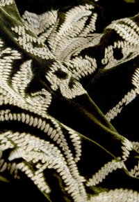 Velvet fabric in deep green with intricate beige embroidery featuring floral patterns and textured accents. Soft and luxurious finish.