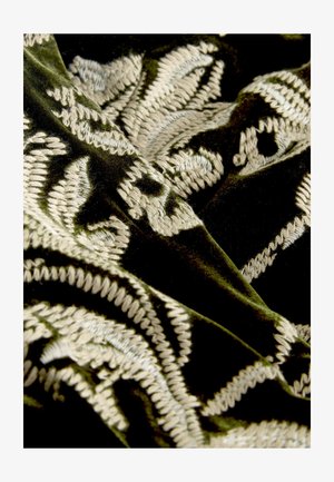 Velvet fabric in deep green with intricate beige embroidery featuring floral patterns and textured accents. Soft and luxurious finish.