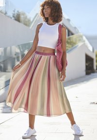 Gonna midi plissettata in tonalità pastello di rosa, verde e beige, con una vita elastica. Abbinata a un crop top bianco e sneakers bianche.