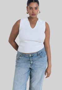 Vit ribbad ärmlös topp med V-ringning, kombinerad med ljusblå löst sittande jeans med en klassisk femficksdesign.