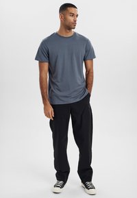 Grå bomulds T-shirt med rund halsudskæring, korte ærmer og regular fit, parret med sorte bukser og sort-hvide sneakers.