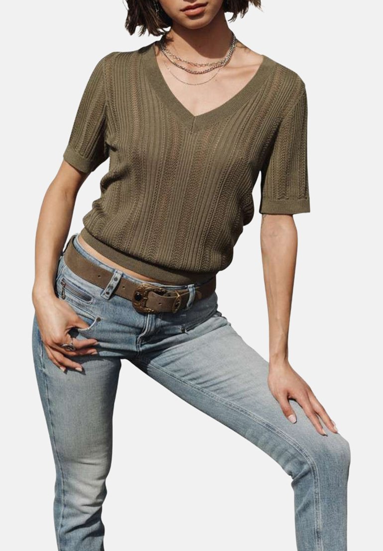 Pull en maille vert olive avec un col en V et des manches courtes, associé à un jean en denim bleu clair et une ceinture marron avec une boucle circulaire.