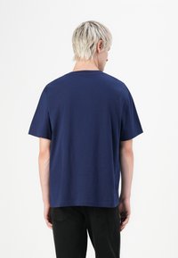 Sötétkék pamut póló rövid ujjal, kerek nyakú és laza szabású. Minimalista design, látható minták vagy logók nélkül.