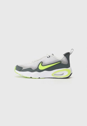 Nike tenisky s šedou síťovinou, bílými a zelenými akcenty, zakřiveným tvarem a viditelnou vzduchovou jednotkou v podrážce, se černou podrážkou.