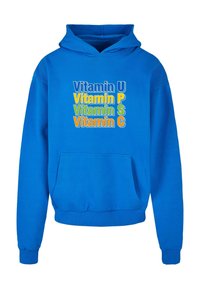 Sudadera azul con cordón, bolsillo frontal y texto gráfico: "Vitamina U", "P", "S" y "C" en varios colores. Tejido suave y corte clásico.