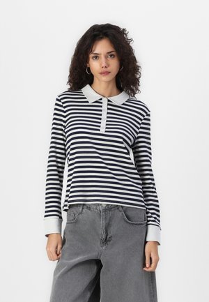 Langermet polo-skjorte i marineblå og hvite striper, med en grå krage, knappestolpe og ribbet tekstur. Kombinert med løse grå bukser.