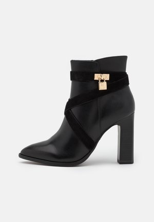 Black leather ankle boot with a pointed toe, suede band, metallic lock detail, and a block heel. Smooth texture with a modern design.