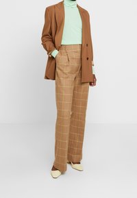 Bruna rutiga byxor med ett gult rutmönster, matchade med en mintfärgad polotröja och en brun blazer. Stylade med krämfärgade spetsiga skor.