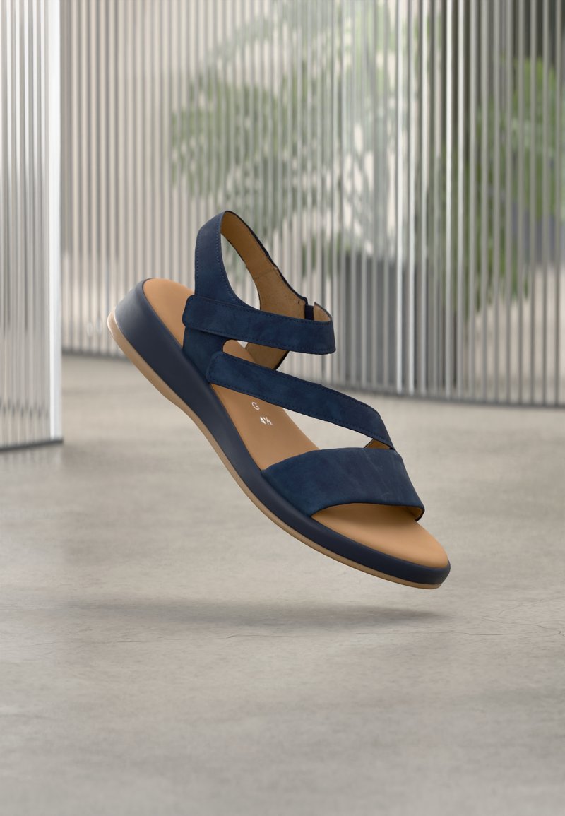 Navy blue sandal with cross straps, made of soft suede. Features a brown footbed and a flexible, dark rubber sole. Lightweight design.