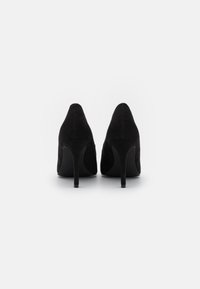 Zapatos de tacón alto de ante negro con diseño de punta afilada, con un delgado tacón stilettto y una textura suave.