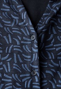 Camicetta blu a fantasia con uno sfondo blu navy e linee astratte di colore azzurro chiaro. Tessuto liscio con chiusura a bottoni classica.