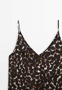 Haut sans manches avec fines bretelles et motif léopard marron et noir sur fond blanc.