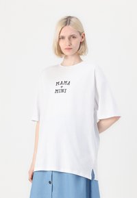 T-shirt en coton blanc à manches courtes et col rond, arborant le texte noir "MAMA + MINI" centré sur le devant.