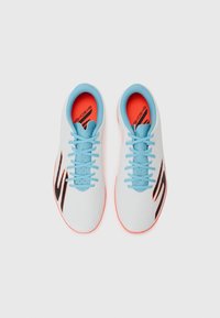 Baskets de sport blanches avec des lacets bleu clair, des accents noirs contrastants et une semelle intérieure orange vif. Tige texturée avec un design épuré.