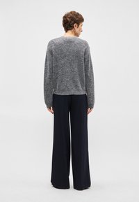 Grijze gebreide trui met lange mouwen, casual pasvorm, gecombineerd met donkere gestreepte wijde broek. Zachte textuur en relaxte silhouet.