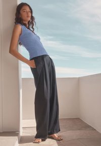 Blue knit sleeveless top with a fitted design, paired with loose-fitting black trousers and flat silver sandals, against a light background.